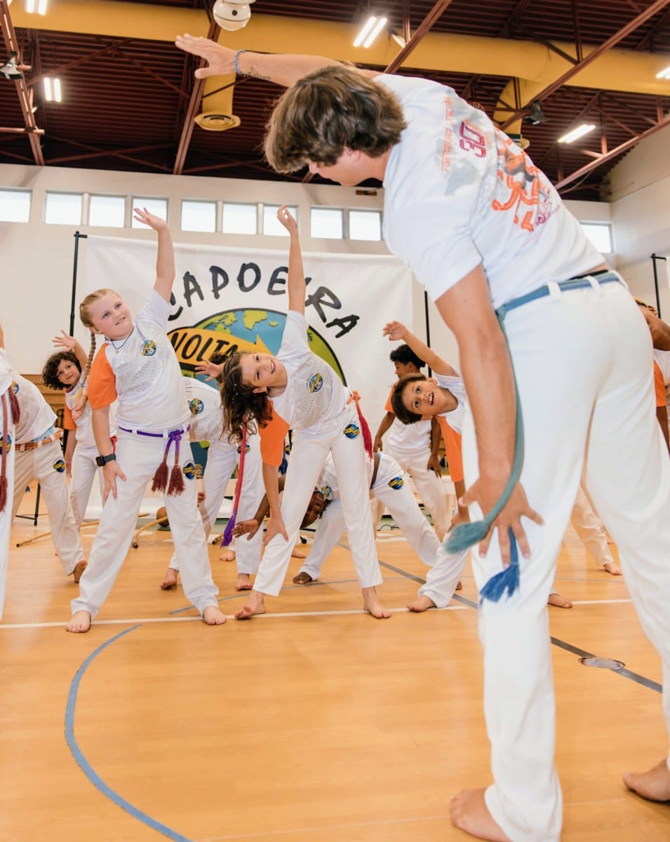 Children stretching with an instructor during a group Capoeira activity.